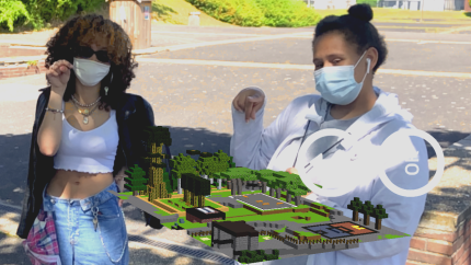 Photo of two women pointing at an Augmented Reality voxel building.